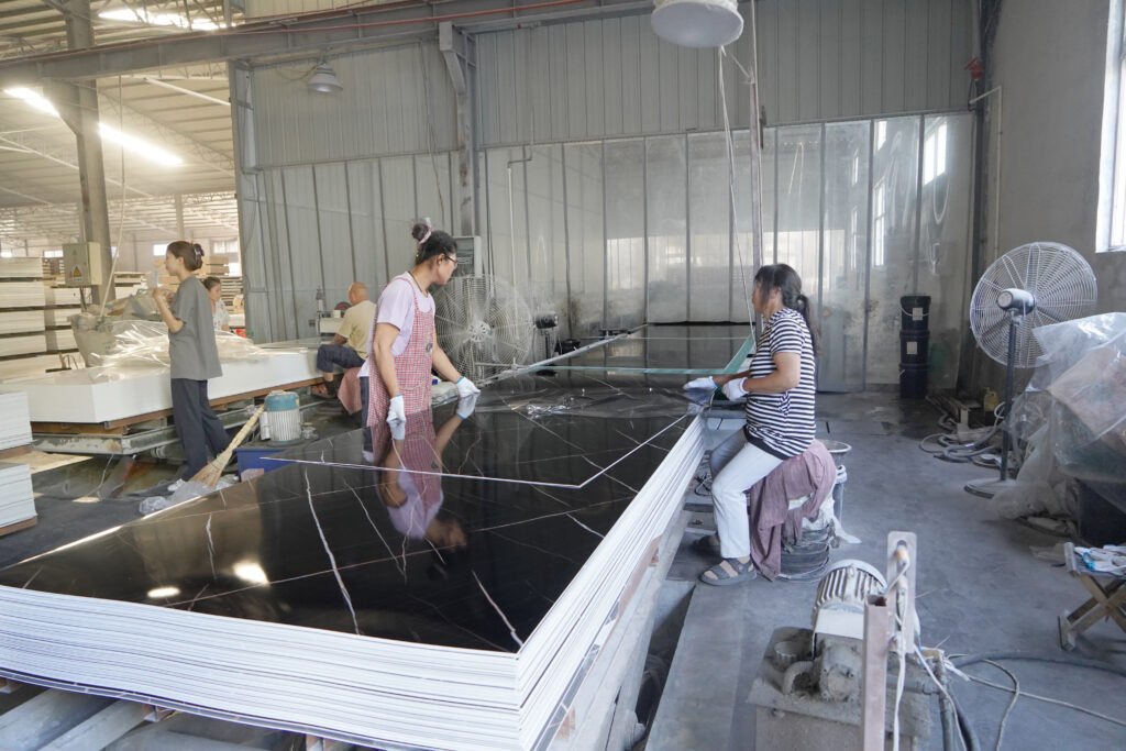 Workers handling surface finishing of black marble pattern PVC marble sheet in factory workshop
